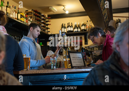 Bianco giovane uomo bar che serve birra a una donna più anziana in un paese di lingua inglese pub su un inverno la giornata con un drink al bar Foto Stock