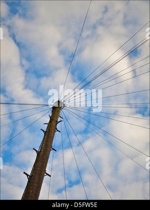 In vecchio stile palo del telefono con linee che corrono per case e passaggi di arrampicata contro un cielo blu Foto Stock