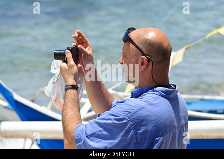 Caucasian uomo di mezza età con testa calva e occhiali da sole sulla sua fronte prende le foto delle vacanze con una Canon point & shoot fotocamera - Sabang, Filippine Foto Stock