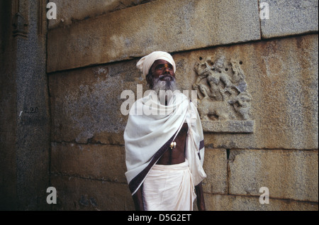 Un Pujari o un sacerdote indù che indossa abiti tradizionali in posa Di fronte ad un antico santuario situato sulla collina di Hemakuta Nell'antico borgo di Hampi annidato tra le rovine Della città medievale di Vijayanagar nello stato di Karnataka In India Foto Stock