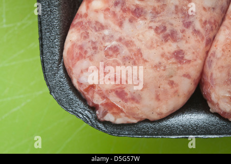 Carne cruda salsiccia, brat,in plastica nera su sfondo verde, Foto Stock