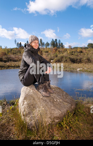 Giovane donna seduta sulle rocce nei pressi di un laghetto. Foto Stock