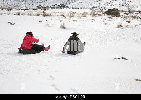 Conwy Galles del Nord marzo due giovani ragazze slittino lungo una coperta di neve via Foto Stock