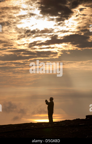 Isola di Man, Snaefell, silhouette dell'uomo prendendo fotografia di vertice al tramonto Foto Stock