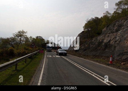 Auto e camion attraversare una strada per riparare il tratto di autostrada nelle Highlands Scozzesi. La strada si restringe significativamente con il segnale di arresto Foto Stock