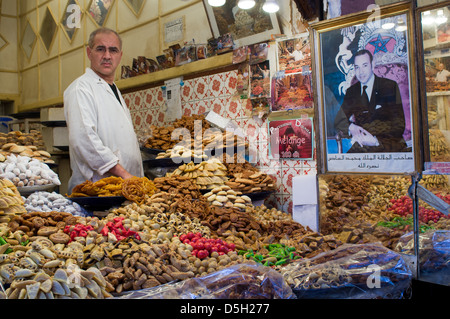 L'uomo vendere i dolciumi e la pasticceria in una fase di stallo nel souk con un ritratto del re, Marrakech, Marocco Foto Stock