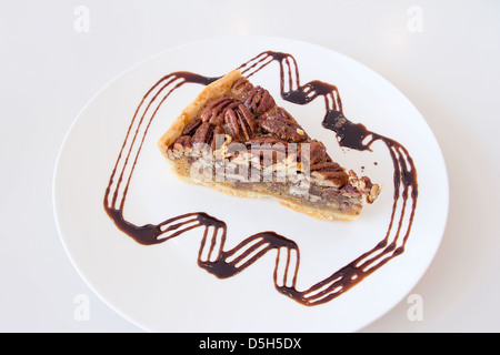 Noci Pecan torta con fetta con cioccolato fondente pioggerella su piastra bianca Foto Stock