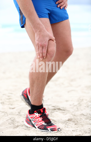 Sezione bassa dei maschi di runner con dolori nelle articolazioni del ginocchio sulla spiaggia Foto Stock