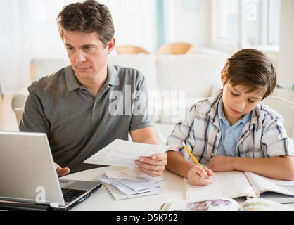 Padre lavora su laptop e figlio (8-9) svolgendo compiti Foto Stock