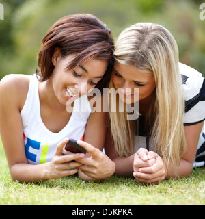 Ritratto di giovane donna giacente su erba, utilizzando il telefono cellulare Foto Stock