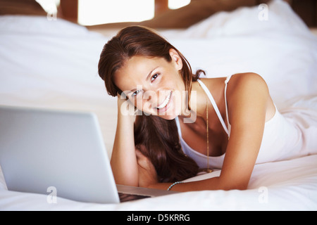 Donna che utilizza computer portatile mentre giaceva a letto Foto Stock