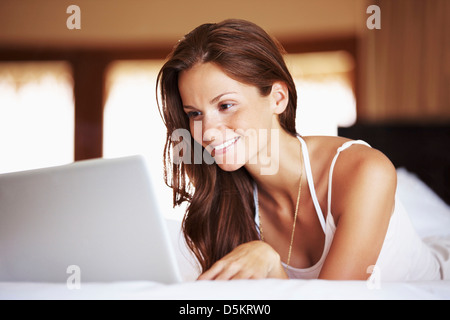 Donna che utilizza computer portatile mentre giaceva a letto Foto Stock