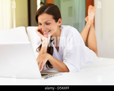 Donna che utilizza computer portatile mentre giaceva sul letto Foto Stock