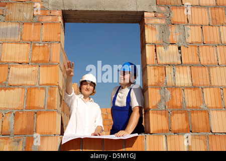 Investitore femmina che mostra il site manager il suo concetto casa all'interno permanente incompiuta casa di mattoni di apertura della finestra Foto Stock