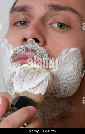 Giovane uomo applicare la crema di rasatura sulla faccia Foto Stock