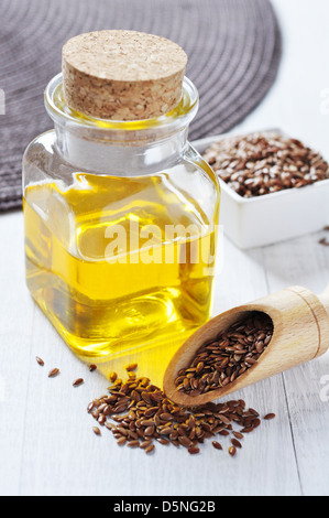 Olio di semi di lino in una bottiglia di vetro e semi di lino su uno sfondo di legno Foto Stock
