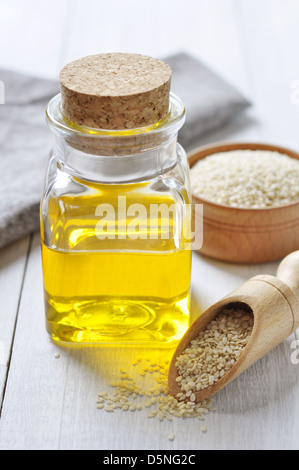 I semi di sesamo e l'olio in una bottiglia di vetro su uno sfondo di legno Foto Stock