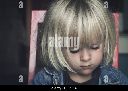 Triste piccolo bambino seduto su una sedia, guardando verso il basso Foto Stock