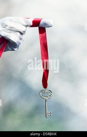 Una mano in guanti bianchi con una vecchia chiave su un nastro rosso Foto Stock