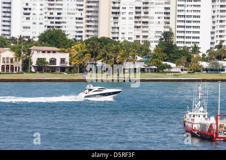 Due uomini su una velocizzazione del bianco e del blu yacht in un canale di spedizione passato condos Foto Stock