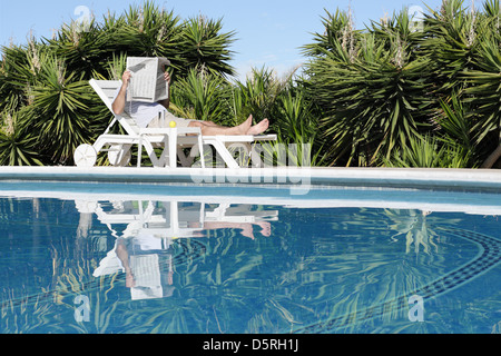 L'uomo rilassante sulla tranquilla piscina e quotidiano di lettura Foto Stock