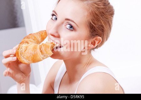 Attraente sorridente giovane donna di mangiare croissant per la colazione Foto Stock