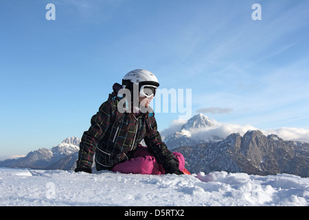 Una giovane ragazza seduta sulla neve nella parte anteriore delle montagne Foto Stock