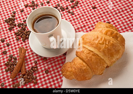 Tazza di caffè con croissant e bastoncini di cannella e i chicchi di caffè sul tavolo. Foto Stock