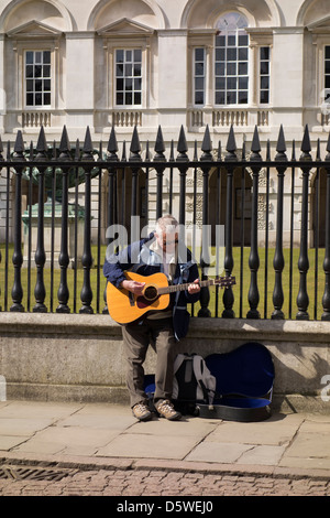 Animatore di strada suonando la chitarra nella parte anteriore della vecchia legge le scuole della città di Cambridge Inghilterra Foto Stock