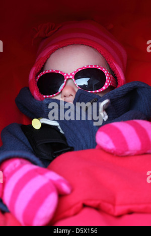 Un bambino indossa sfumature, guanti e un cappello. Foto Stock