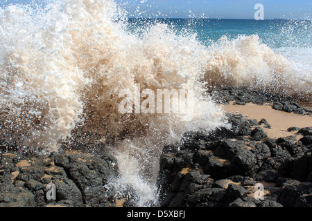 Onde dell'Oceano Indiano la rottura e la zangolatura sul buio rocce basaltiche che invio a spruzzo di sabbia in alto l'aria . Foto Stock