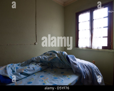 Letto disfatto in una camera oscura Foto Stock