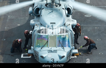 US Navy marinai guarnitura e catena un MH-60S Knight Hawk elicottero sul ponte di volo della portaerei USS Nimitz Aprile 4, 2013 nell'Oceano Pacifico. Foto Stock