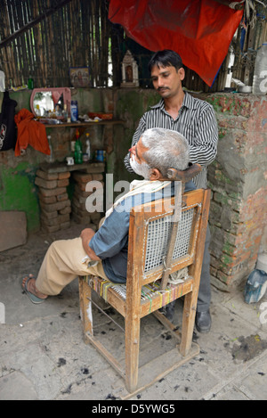 Un cliente avente una faccia di rasatura nel realizzare localmente un negozio da barbiere in una strada laterale di Nuova Delhi in India Foto Stock