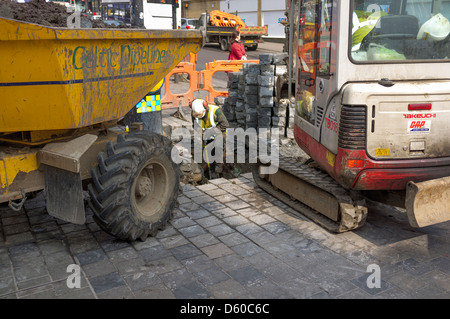 Workman di scavare un buco in un marciapiede con una pala e un piccolo JCB, Glasgow, Scozia Foto Stock