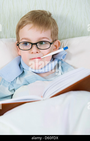 Malati little boy giacente a letto con il termometro e leggere prenota Foto Stock