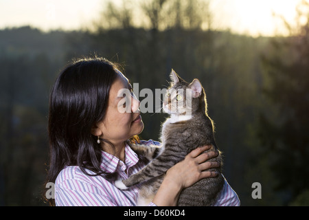 Foto orizzontale di donna matura azienda cat all aperto con fading tramonto e alberi in background Foto Stock