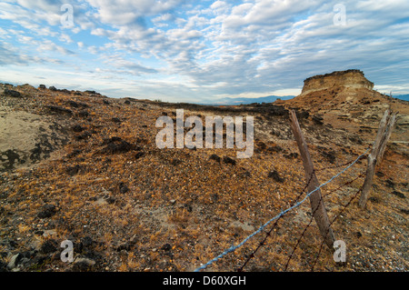 Recinzione che si estende in un roccioso deserto sterile sotto un cielo drammatico Foto Stock