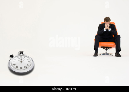 Preoccupato per il businessman seduta con cronometro che rappresenta la perdita di tempo Foto Stock