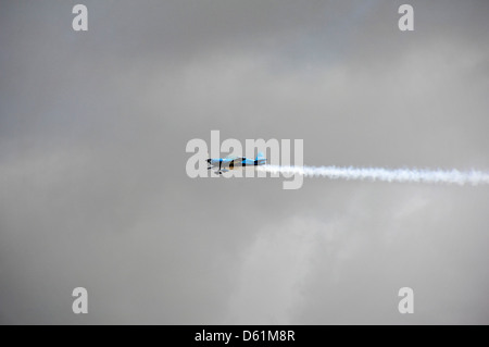 Vista orizzontale di un Extra Flugzeugbau EA300 monoplan vola con un sentiero di vapori durante un display dell'aria. Foto Stock