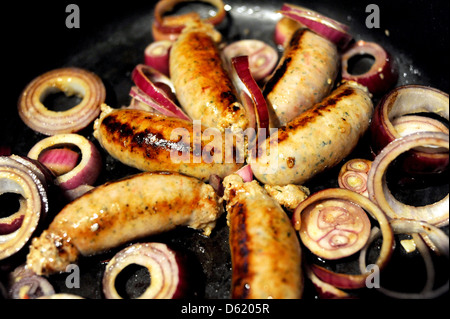 Salsicce di maiale sfrigolanti in padella con le cipolle rosse come essi vengono cotti per pasto Foto Stock