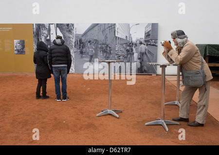 Visitatori imparare circa il muro di Berlino leggere outdoor pannelli espositivi nei pressi dell'ex Checkpoint Charlie, l'ex confine comunista tra Berlino Ovest e Berlino Est durante la Guerra Fredda. Il muro di Berlino è stata una barriera costruita dalla Repubblica democratica tedesca, la Germania Est) a partire dal 13 agosto 1961, che completamente tagliata (via terra) a Berlino Ovest dal circostante della Germania orientale e di Berlino Est. (Di più nella descrizione) .. Foto Stock