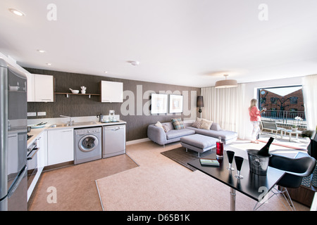 Una giovane donna caucasica gustando un bicchiere di vino, guardando fuori della finestra dal suo soggiorno. Foto Stock