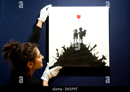 Londra, Regno Unito. Il 12 aprile 2013. Un assistente vendite detiene una tela intitolata "I bambini su Guns' da Banksy durante il 'Arte Urbana' anteprima di aste Bonhams a. "I bambini sulle armi da fuoco" è un esempio di artista più in clima politico, questa tela, che raramente appare in asta, viene offerto a £ 50,000-70,000. Come molti di Banksy più famose creazioni, a prima vista la pittura può sembrare piuttosto dolce, ma sulle ispezioni più stretta la sua visione è molto più funesta. Credito: Piero Cruciatti / Alamy Live News Foto Stock