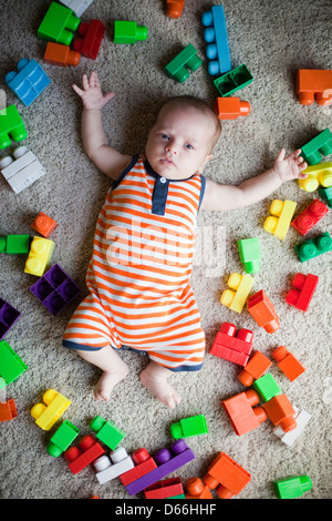 Neonato sdraiato sul pavimento circondato da giocattoli Foto Stock