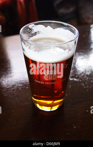 Una pinta di birra stampato bicchiere di Batemans amara su un bar pub tavola bicchieri di bevande Foto Stock