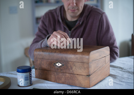 Uomo di mezza età a un tavolo da cucina ripristina un antico stile vittoriano pendenza di scrittura pronti a vendere ad una asta o negozio di antiquariato Foto Stock