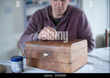 Uomo di mezza età a un tavolo da cucina ripristina un antico stile vittoriano pendenza di scrittura pronti a vendere ad una asta o negozio di antiquariato Foto Stock