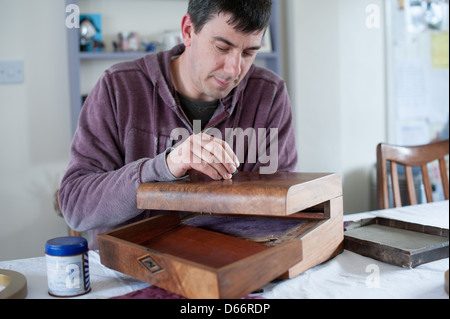 Uomo di mezza età a un tavolo da cucina ripristina un antico stile vittoriano pendenza di scrittura pronti a vendere ad una asta o negozio di antiquariato Foto Stock