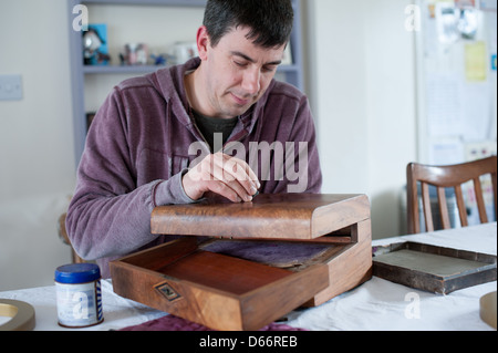 Uomo di mezza età a un tavolo da cucina ripristina un antico stile vittoriano pendenza di scrittura pronti a vendere ad una asta o negozio di antiquariato Foto Stock